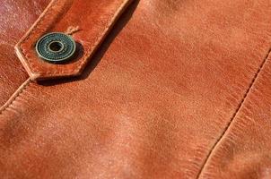 Brown leather texture. Useful as background for any design work. Macro photo of a button on outer clothing made of genuine leather