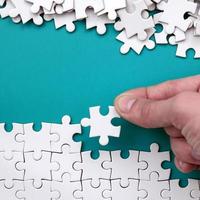 The hand folds a white jigsaw puzzle and a pile of uncombed puzzle pieces lies against the background of the blue surface. Texture photo with space for text
