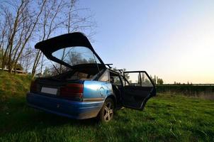 A blue car on a background of a rustic landscape with a wild cane field and a small lake. The family came to rest on the nature near the lake photo