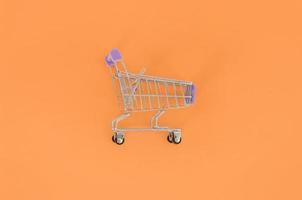 adicción a las compras, amante de las compras o concepto de adicto a las compras. un pequeño carrito de compras vacío se encuentra sobre un fondo de papel de color pastel. composición mínima plana, vista superior foto