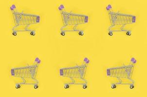 Shopping addiction, shopping lover or shopaholic concept. Many small empty shopping carts perform a pattern on a pastel colored paper background. Flat lay composition, top view photo