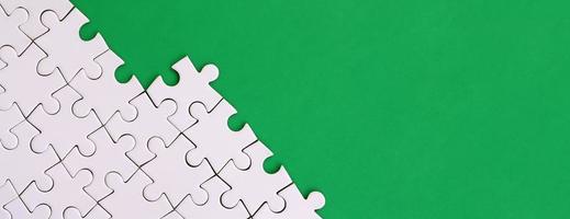 Fragment of a folded white jigsaw puzzle on the background of a green plastic surface. Texture photo with copy space for text