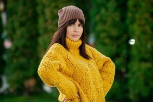 Beautiful European brunette dressed in a yellow woolen sweater and hat outside. The beautiful girl who wears thick stylish autumn clothes in cool weather. photo