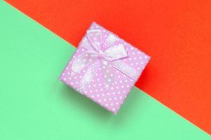 Small pink gift box lie on texture background of fashion pastel turquoise and red colors paper photo