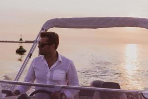 un hombre de negocios de alto nivel decidido con ropa informal y gafas de sol disfruta de sus vacaciones conduciendo un barco de lujo al atardecer. enfoque selectivo foto