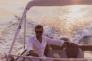 A determined senior businessman in casual clothes and sunglasses enjoys his vacation driving a luxury boat at sunset. Selective focus photo