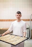 A young baker holding raw product of white dough photo