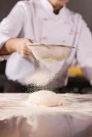 chef sprinkling flour over fresh pizza dough photo