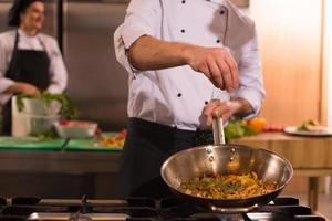 chef putting spices on vegetables in wok photo