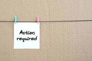 Action required Note is written on a white sticker that hangs with a clothespin on a rope on a background of brown cardboard photo