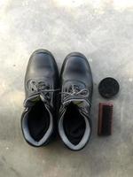 Black safety shoes next to a shoe brush and shoe polish photo