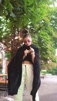 Woman outside wearing black poncho top purple oval sunglasses and a top bun video