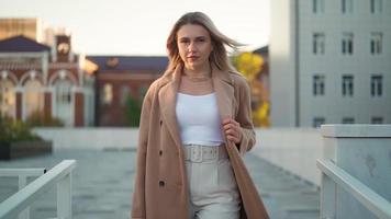 retrato, atractiva mujer de negocios que se ve confiada en un abrigo marrón está caminando por una calle de la ciudad. gente de carrera belleza de la moda. retratos femeninos. gente real. camara lenta video