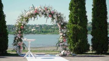 lugar para la ceremonia nupcial en color blanco contra el fondo del río. arco de boda con ramos de rosas pastel. camara lenta video