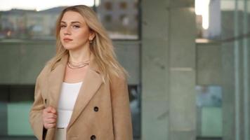 Portrait, Pretty Blonde Business Woman Looking Confident in Brown Coat Stands on Background Office Building in City Center. Career People. Fashion, Beauty. Female Portraits. Real People. Slow Motion video