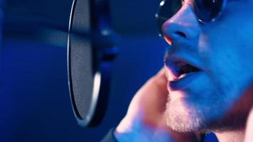 cantante de rap masculino con auriculares canta hip hop en un micrófono. creación de una nueva canción en un estudio de grabación profesional con un ingeniero de sonido. trabajar en la sala de grabación de música. video