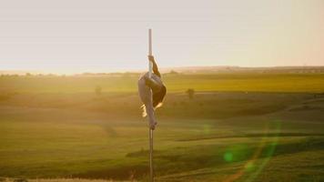 Sportliche Frau führt akrobatische Stunts auf einer Stange vor dem Hintergrund eines wunderschönen Sonnenuntergangs durch. Sport und Motivation. gesunder Lebensstil. Freiheit. Zeitlupe video