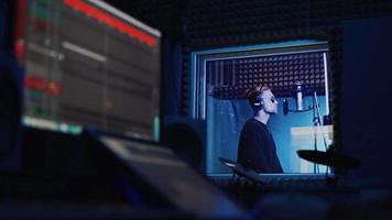 manlig rap sångare med hörlurar och ljud ingenjör är skapande en ny låt i professionell inspelning studio. program och verktyg för skapande musik på dator övervaka. arbete i de musik inspelning rum