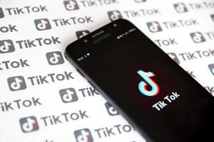 ternopil, ucrania - 2 de mayo de 2022 aplicación de teléfono inteligente tik tok en pantalla y muchos logotipos de tiktok impresos en papel. tiktok o douyin es un famoso servicio chino de alojamiento de videos de formato corto propiedad de bytedance foto