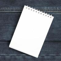 White notebook with clean pages lying on dark blue jeans background. Image with copy space photo