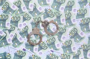 Police handcuffs lies on a set of green monetary denominations of 100 euros. A lot of money forms an infinite heap photo