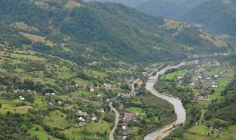 A beautiful view of the village of Mezhgorye, Carpathian region. A lot of residential buildings surrounded by high forest mountains and long river photo