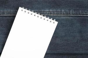 White notebook with clean pages lying on dark blue jeans background. Image with copy space photo