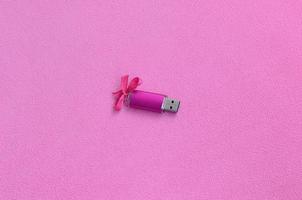 la tarjeta de memoria flash usb de color rosa brillante con un lazo rosa yace sobre una manta de suave y peluda tela de vellón rosa claro. diseño clásico de regalo femenino para una tarjeta de memoria foto