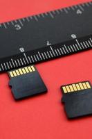 Two small micro SD memory cards lie on a red background next to a black ruler. A small and compact data and information store photo