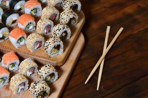 A detailed shot of a set of Japanese sushi rolls and a device for their use chopsticks , which are located on a wooden cutting board on a table in the kitchen of a sushi bar photo