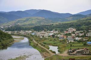 A beautiful view of the village of Mezhgorye, Carpathian region. A lot of residential buildings surrounded by high forest mountains and long river photo