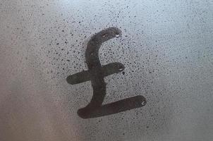 Symbol of English pounds is written with a finger on the surface of the misted glass photo