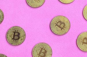 muchos bitcoins dorados se encuentran sobre una manta hecha de suave y esponjosa tela de lana rosa claro. visualización física de moneda criptográfica virtual foto