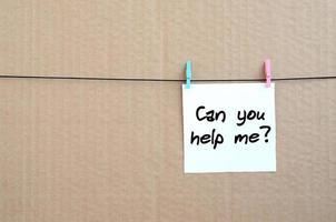 Can you help me Note is written on a white sticker that hangs with a clothespin on a rope on a background of brown cardboard photo