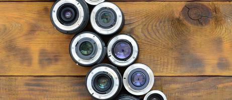 Several photographic lenses lie on a brown wooden background. Space for text photo