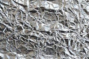 Thin wrinkled sheet of crushed tin aluminum silver foil background with shiny crumpled surface for texture photo