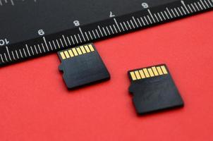 Two small micro SD memory cards lie on a red background next to a black ruler. A small and compact data and information store photo