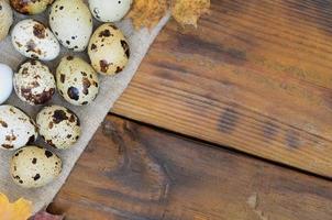 Quail eggs with autumn leaves on sacking on a dark brown wooden surface, top view, empty place for text, recipe photo