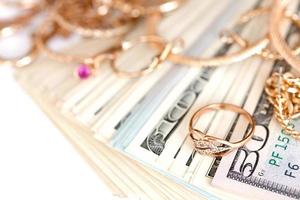 muchos costosos anillos, aretes y collares de joyería dorada con una gran cantidad de billetes de dólares estadounidenses sobre fondo blanco. casa de empeño o joyería foto