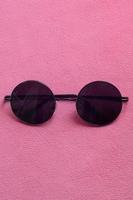 elegantes gafas de sol negras con gafas redondas se encuentran sobre una manta hecha de suave y esponjosa tela de lana rosa claro. imagen de fondo de moda en colores femeninos foto