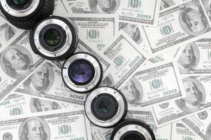 A few photographic lenses lies on the background of a lot of dollar bills. Space for text photo