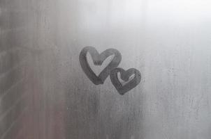 un par de símbolos de corazón de amor borrosos abstractos dibujados a mano en el cristal húmedo de la ventana con fondo de luz solar. plantilla para tarjetas postales del día de san valentín foto