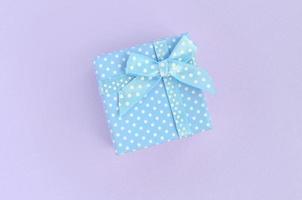 Small blue gift box with ribbon lies on a violet background. Minimalism flat lay top view photo