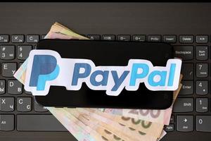 TERNOPIL, UKRAINE - SEPTEMBER 6, 2022 Payoneer paper logotype lies on black laptop with ukrainian hryvnia bills. Payoneer is American financial services company provides online money transfer photo