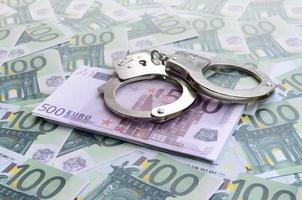 Police handcuffs lies on a set of green monetary denominations of 100 euros. A lot of money forms an infinite heap photo