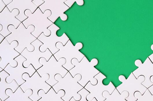 Fragment of a folded white jigsaw puzzle on the background of a green plastic surface. Texture photo with copy space for text