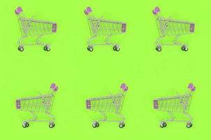 Shopping addiction, shopping lover or shopaholic concept. Many small empty shopping carts perform a pattern on a pastel colored paper background. Flat lay composition, top view photo