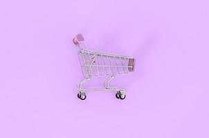 adicción a las compras, amante de las compras o concepto de adicto a las compras. un pequeño carrito de compras vacío se encuentra sobre un fondo de papel de color pastel. composición mínima plana, vista superior foto