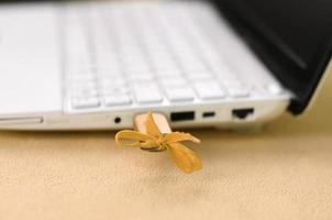 An orange USB flash drive with a bow is connected to a white laptop, which lies on a blanket of soft and fluffy light orange fleece fabric. Classic female design for a memory card photo