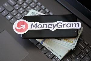 TERNOPIL, UKRAINE - SEPTEMBER 6, 2022 MoneyGram paper logotype lies on black laptop with US dollar bills. Moneygram is American cross border P2P payments and money transfer company photo